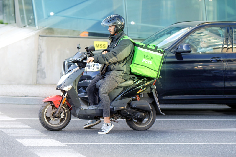 19 - An Uber Eats delivery courier riding a scooter with an insulated green delivery backpack
